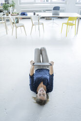 Portrait of laughing young woman with tablet lying on the floor in a loft - JOSF02141