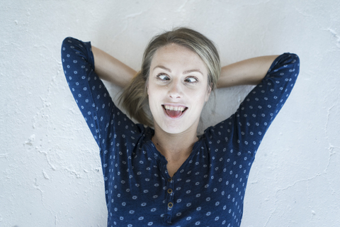 Porträt einer jungen Frau, die auf dem Boden liegt und komische Gesichter zieht, lizenzfreies Stockfoto