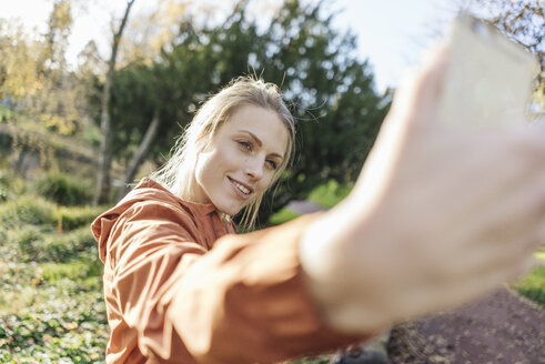 Porträt einer jungen Frau, die ein Selfie mit ihrem Handy in einem herbstlichen Park macht - JOSF02153