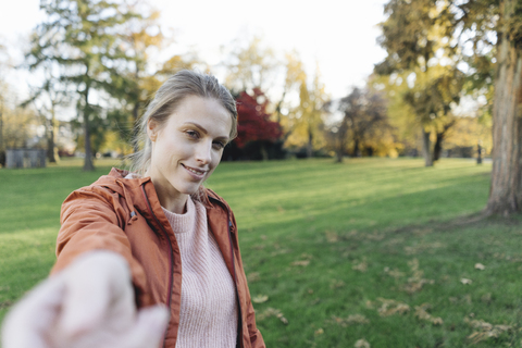 Porträt einer jungen Frau mit ausgestreckter Hand in einem herbstlichen Park, lizenzfreies Stockfoto