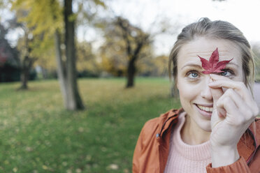 Portrait of young woman with autumn leaf in a park - JOSF02157