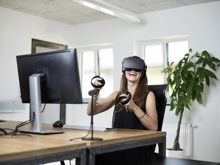 Glückliche Frau mit VR-Brille am Schreibtisch im Büro - CVF00017