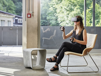 Smiling woman wearing VR glasses sitting on chair - CVF00019