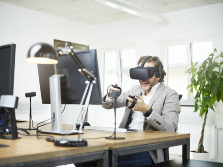 Glücklicher Mann mit VR-Brille am Schreibtisch im Büro - CVF00022