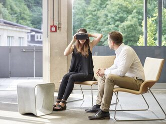 Man looking at woman wearing VR glasses sitting on chair - CVF00026