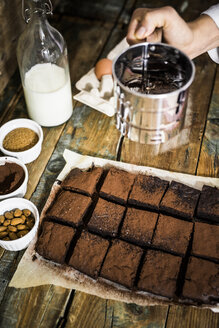 Frauenhand, die Kakao auf Brownies streut - GIOF03745