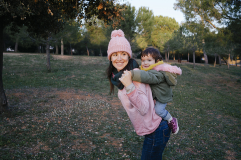 Happy mother carrying little daughter piggyback on a meadow stock photo