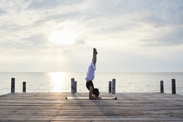 Young woman practicing yoga on a jetty by the sea at sunset - IGGF00390