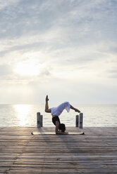 Junge Frau übt Yoga auf einem Steg am Meer bei Sonnenuntergang - IGGF00391