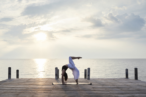 Young woman practicing yoga on a jetty by the sea at sunset stock photo