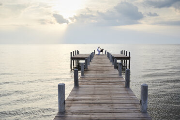 Young woman practicing yoga on a jetty by the sea at sunset - IGGF00394