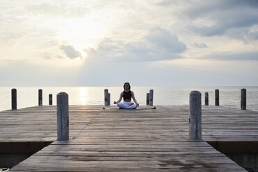Junge Frau übt Yoga auf einem Steg am Meer bei Sonnenuntergang - IGGF00395