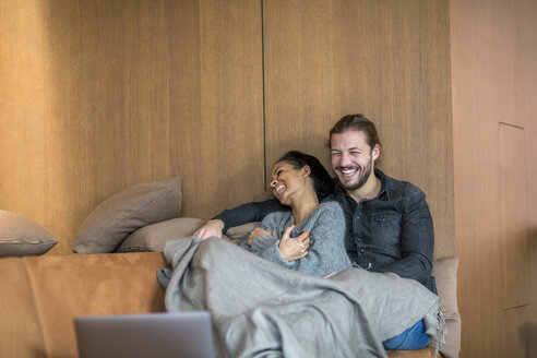 Lachendes junges Paar entspannt sich zusammen auf der Couch - FMKF04684