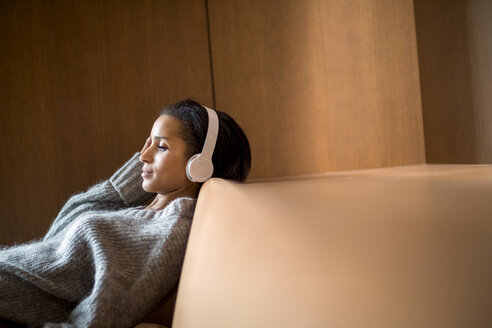 Porträt einer entspannten jungen Frau, die mit Kopfhörern auf der Couch Musik hört - FMKF04686