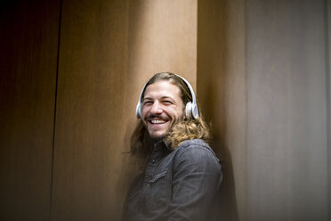 Porträt eines lachenden Mannes, der mit Kopfhörern Musik hört - FMKF04687