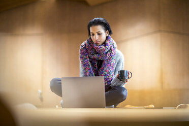 Porträt einer modischen jungen Frau mit einer Tasse Kaffee, die am Konferenztisch sitzt und einen Laptop benutzt - FMKF04691