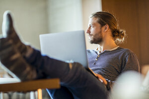 Porträt eines nachdenklichen jungen Mannes am Laptop - FMKF04718