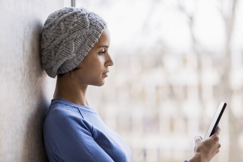 Porträt einer jungen Frau vor einem Fenster mit Blick auf ein Handyfenster - FMKF04730