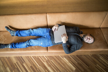 Mann mit Laptop entspannt auf Couch - FMKF04738