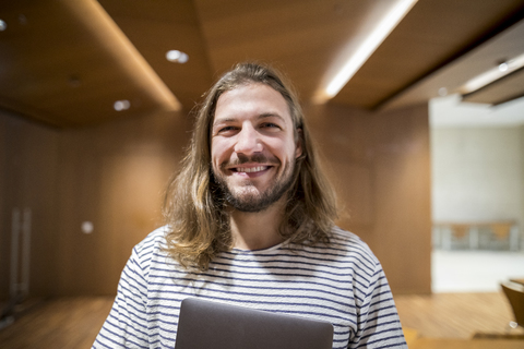 Porträt eines lachenden Mannes mit Laptop in der Universität, lizenzfreies Stockfoto