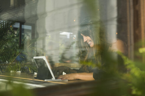 Lächelnde Frau mit Tablet in einem Café hinter einem Fenster - SBOF01176