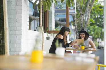Zwei lächelnde Frauen teilen ein Tablet vor einem Café - SBOF01183