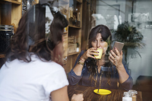 Frau mit Freundin in einem Café, die ein Smartphone hält und Kaffee trinkt - SBOF01184