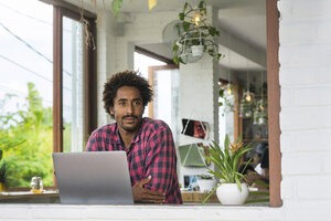 Mann sitzt in einem Café vor einem Fenster mit Laptop - SBOF01187