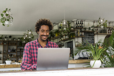 Smiling man using laptop in a cafe - SBOF01190