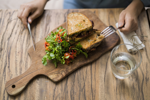 Hände halten Messer und Gabel an einem Holztisch mit dekoriertem Salat und knusprigem Brot, lizenzfreies Stockfoto