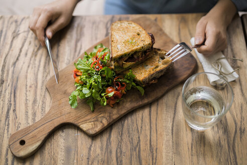 Hände halten Messer und Gabel an einem Holztisch mit dekoriertem Salat und knusprigem Brot - SBOF01196