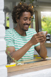 Smiling man checking his smartphone at the bar in a cafe - SBOF01226