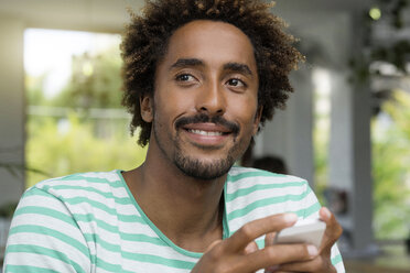 Smiling man with smartphone in a cafe - SBOF01227