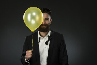 Portrait of a young man holding a balloon, wearing loose black tie - MAEF12492