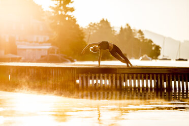 Woman practicing yoga on jetty at a lake - DAWF00562