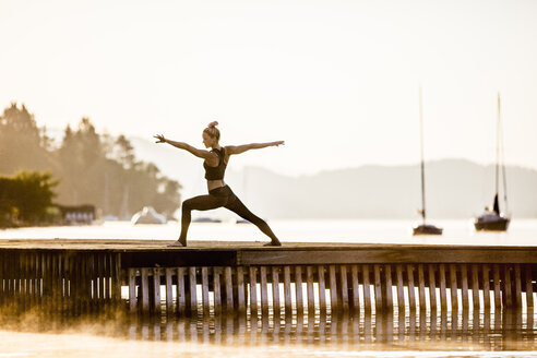 Frau übt Yoga auf einem Steg an einem See - DAWF00563