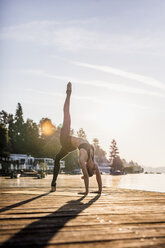 Woman practicing yoga on jetty at a lake - DAWF00570