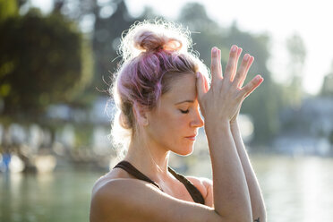 Frau mit gefärbtem Haar meditiert an einem See - DAWF00572