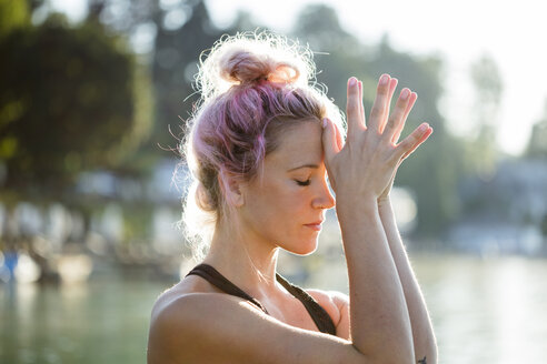 Woman with dyed hair meditating at a lake - DAWF00572