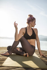 Frau sitzt auf einem Steg an einem See und übt Yoga - DAWF00575