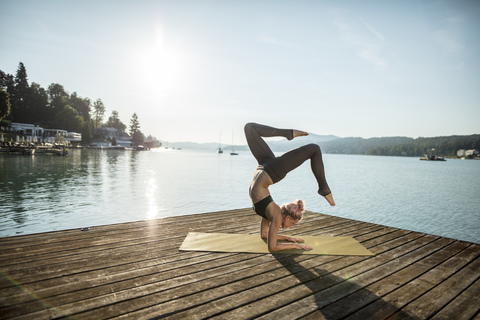 Frau übt Yoga auf einem Steg an einem See, lizenzfreies Stockfoto