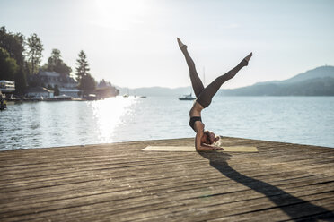 Woman practicing yoga on jetty at a lake - DAWF00579