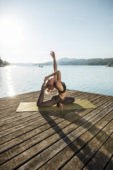 Frau übt Yoga auf einem Steg an einem See - DAWF00581