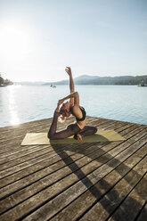 Woman practicing yoga on jetty at a lake - DAWF00581