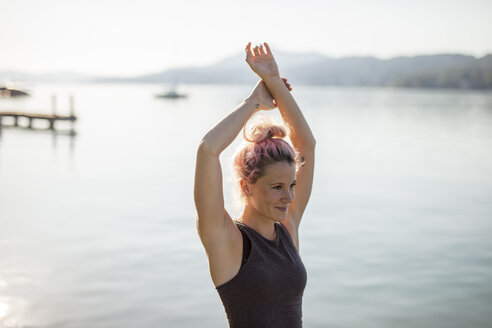 Frau in Sportkleidung beim Stretching an einem See - DAWF00585