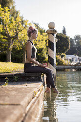 Frau in Sportkleidung am Seeufer sitzend mit den Füßen im Wasser - DAWF00587