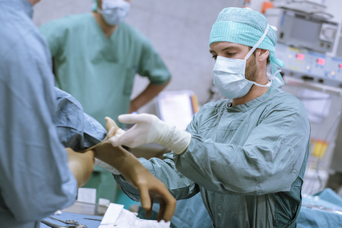 Assistentin hilft dem Chirurgen beim Anziehen des Handschuhs vor einer Operation, lizenzfreies Stockfoto