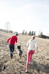 Mann und Frau mit Hund laufen auf einem Feld - ECPF00178