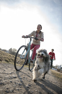 Mann und Frau mit Hund fahren Fahrrad auf einem Feldweg - ECPF00179