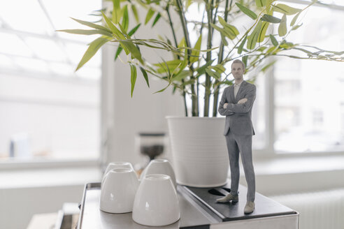 Miniature businessman figurine standing on coffee machine in office - FLAF00115